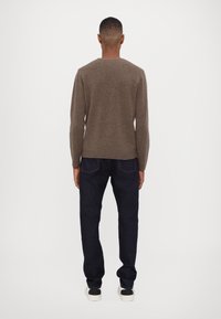 Brown knitted sweater paired with dark blue jeans. The sweater features a round neckline and ribbed cuffs and hem. Sneakers with black accents.