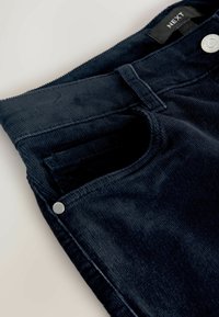 Marineblå corduroy bukser med lynlås og knaplukning. Har en frontlomme og en blød, struktureret overflade. Etiketten viser "NEXT."