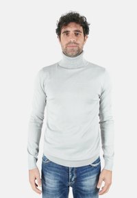 Maglione a collo alto grigio chiaro in morbido tessuto lavorato a maglia, design aderente con collo e polsini a coste, indossato con jeans blu strappati.