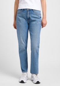 Lichtblauwe spijkerbroek met rechte pasvorm, vijfzakkenontwerp en subtiele vervaging. Gecombineerd met witte sportschoenen.