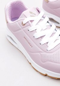 Sneaker Skechers rosa chiaro con lacci bianchi, dettagli perforati e accenti dorati. Suola imbottita con suola in gomma a contrasto.