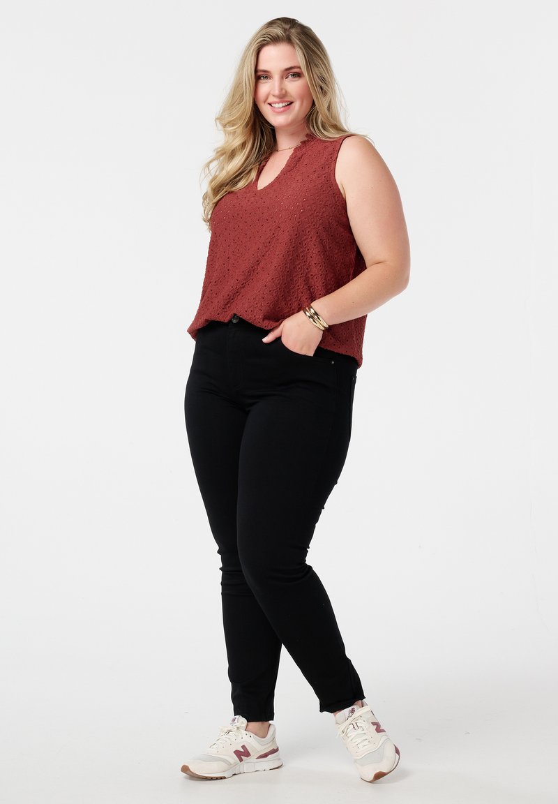 Roestkleurig mouwloos topje met een textuurpatroon, gecombineerd met hoge zwarte jeans en witte sneakers met roze accenten.