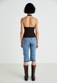 Top în nuanță de maro cu bretele, purtat cu pantaloni capri din denim de culoare albastră deschisă și cizme maro până la genunchi. Material neted, design ajustat, siluetă relaxată din denim.