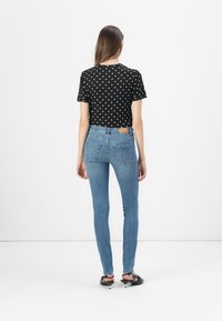 Black polka dot short-sleeve top paired with blue skinny jeans, showing a fitted design; model turned away from the camera.