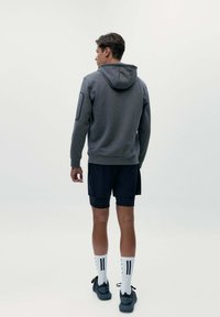 Šedá mikina s kapucňou, dlhými rukávmi a textúrovaným povrchom, skombinovaná s čiernymi šortkami a bielymi ponožkami s čiernymi pruhmi.