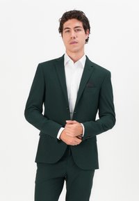 Dark green suit with a tailored fit, features a notch lapel, single-button closure, and a white dress shirt underneath.