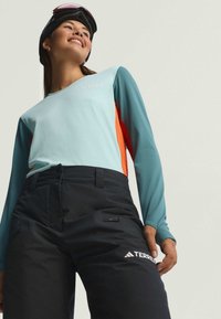Svetlomodré a oranžové tričko s dlhým rukávom kombinované s čiernymi nohavicami, s bočnou zipsovou vreckom a logom na stehne. Hladká tkanina, športový dizajn.