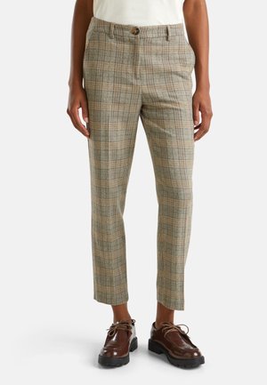 Personne portant un pantalon beige à carreaux sur mesure avec des poches latérales, des chaussures marron en cuir à lacets, et un haut blanc rentré.