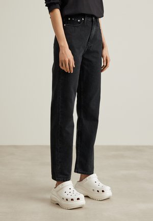 Pantalones rectos de mezclilla negra con cinco bolsillos, cierre frontal con botón y zuecos blancos de plataforma con agujeros de ventilación.
