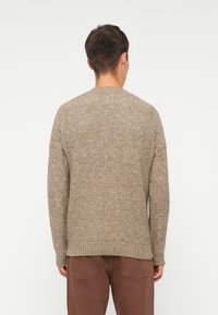 Brown textured knit sweater with a round neckline and ribbed hem, paired with dark brown pants. Back view shows the garment's fit and material.