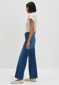 Lichte wijdvallende blauwe spijkerbroek van denim, met een hoge taille, vijf zakken en een klassieke blauwe wassing; gecombineerd met een lichtgekleurde geribbelde top.