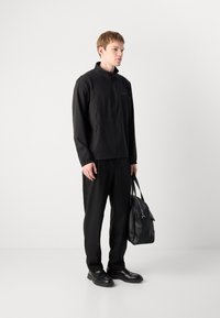 Čierna ľahká bunda s vysokým golierom, zapínaním na zips a dvoma bočnými vreckami, v kombinácii s čiernymi nohavicami a elegantnou koženou taškou.