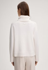Weißer, gestrickter Pullover mit hohem Rippkragen, überschnittenen Schultern und einem Knopfdetail auf der Rückseite. Hat eine lässige, kastige Passform.