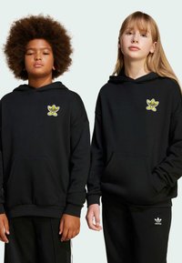 Černé mikiny s kapucí a předními kapsami, s žebrovanými manžetami, zdobené žlutou karikaturou květiny na levé části hrudi. Nosené s odpovídajícími černými kalhotami.