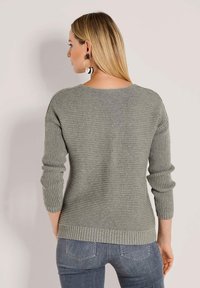 Grauer Strickpullover mit strukturiertem Rippdesign, Rundhalsausschnitt und langen Ärmeln. Getragen mit blauen Jeans.