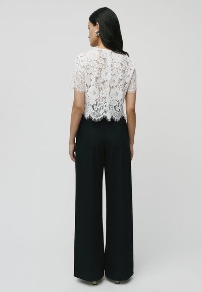 Witte kanten crop top met korte mouwen en golvende zoom, gecombineerd met hoge taille zwarte wijde broek. Gelaagd bloemmotief.