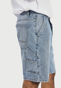Shorts de mezclilla en azul claro con un ajuste relajado. Presentan múltiples bolsillos, costuras visibles y un corte recto en el dobladillo.
