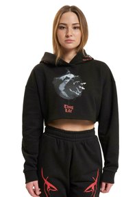 Black cropped hoodie with bear graphic and red text "Thug Life," featuring a drawstring hood and long sleeves. Paired with black sweatpants.