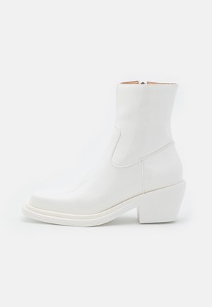 Bottines en cuir verni blanc, avec un bout arrondi et un talon bloc. Présentent un design épuré et des panneaux élastiques sur les côtés pour un enfilage facile.