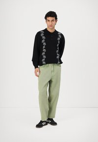 Black long-sleeve polo with white floral embroidery on the front, paired with light green wide-leg pants and black sneakers.