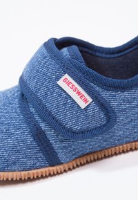 Niebieski but tekstylny z wzorem przypominającym dżins, z zapięciem na rzep i gumową podeszwą z teksturowanym gripem. Widoczna metka z logo.