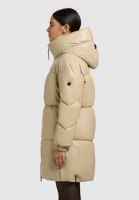 Béžová prešívaná bunda s vysokým golierom, prešívaným dizajnom, elastickými manžetami a bočnými zipsami. Vyrobená z hladkého, ľahkého materiálu.