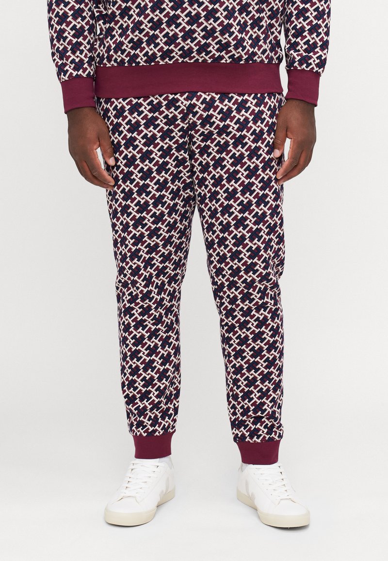 Navy en bordeaux gemusterde joggers met een geometrisch ontwerp, afgewerkt met boorden bij de enkels en gecombineerd met witte sneakers. Gladde stofstructuur.