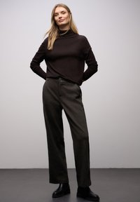 Maglione nero a collo alto con maniche lunghe, abbinato a pantaloni grigi a vita alta con motivo e stivali neri alla caviglia. Silhouette semplice e moderna.