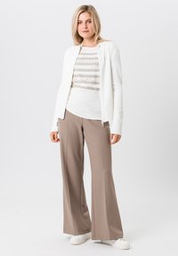 Witte rits-cardigan over een lichtbeige gestreept T-shirt, gecombineerd met beige wijde broek en witte sneakers. Gladde textuur, moderne pasvorm.