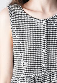 Zwart-wit gestreepte mouwloze jurk met een ronde halslijn, voorzien van knoopsluitingen en een geruffelde zoom, gemaakt van textuurstof.