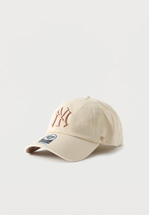 Beige cotton baseball cap with a curved brim, featuring an embroidered NY logo in pale pink and a tag on the front panel.
