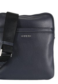 Borsa a tracolla in pelle blu navy con finitura testurizzata. Caratterizzata da una tracolla nera regolabile e dal logo "GUESS" in argento sul davanti.