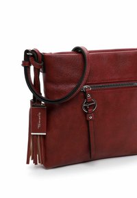 Red leather crossbody bag with a zippered pocket, circular hardware accent, detachable tassel, and a textured finish.