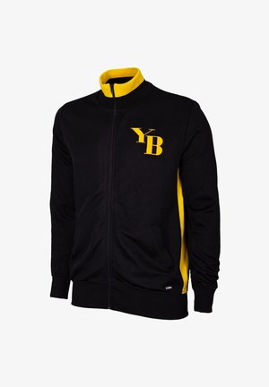 Zwarte zip-up jas met gele accenten, geribbelde kraag en manchetten. Bevat een geel "YB" logo op de linkerkant van de borst. Zachte stofstructuur.