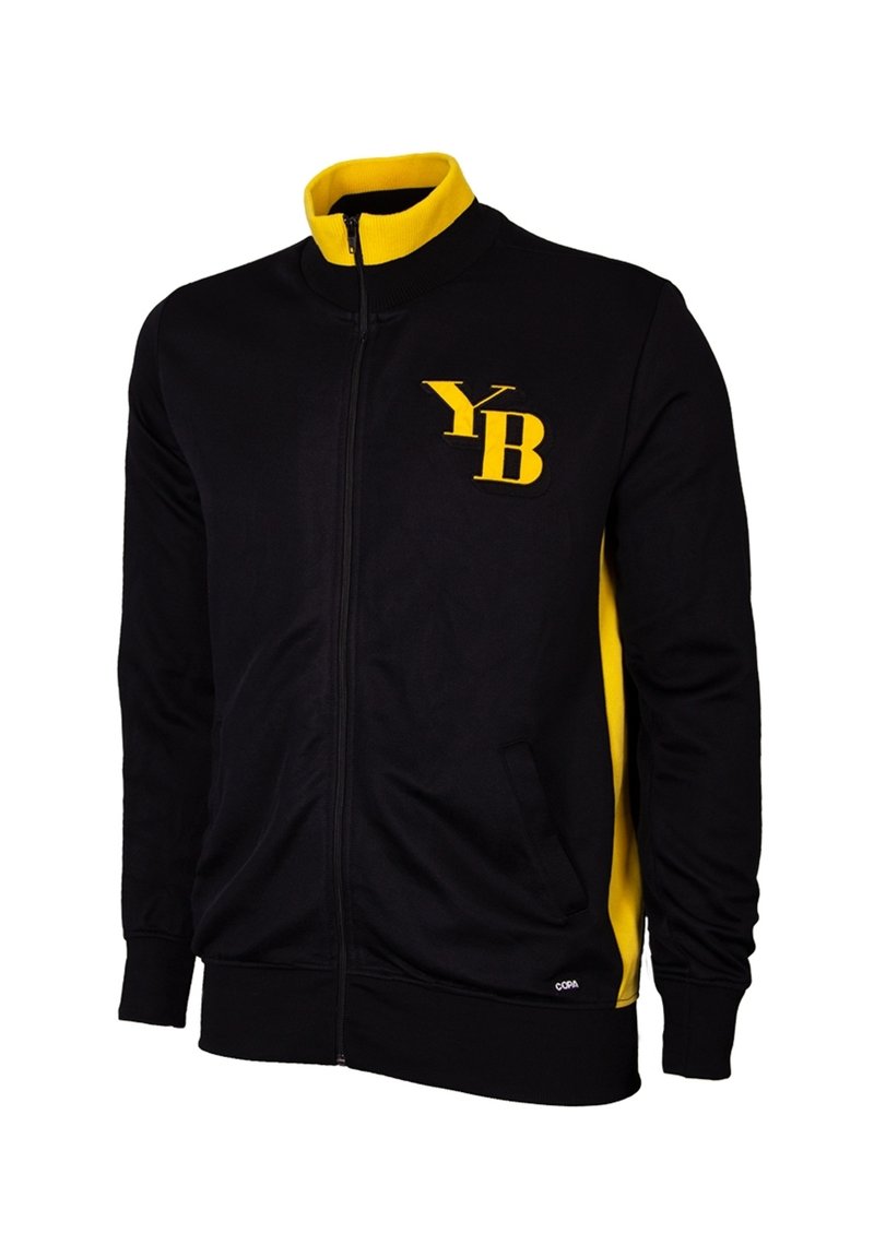 Zwarte zip-up jas met gele accenten, geribbelde kraag en manchetten. Bevat een geel "YB" logo op de linkerkant van de borst. Zachte stofstructuur.