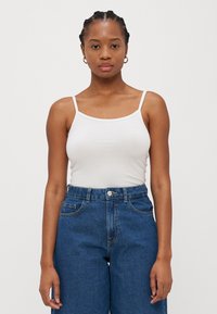 Hvit tettsittende tank topp med tynne stropper, kombinert med høy midje lyseblå denimbukser. Glatt tekstur, minimalistisk design, klassiske farger.