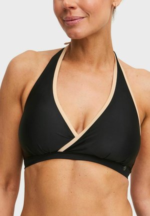 Vrouw met zwarte halterbikinitop met beige rand, zichtbaar bovenlichaam en nek, met een lichte glimlach.