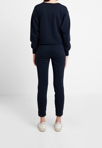 Sudadera azul marino y joggers a juego, hechos de una tela suave con un corte holgado. La sudadera cuenta con mangas largas, joggers hasta los tobillos y zapatillas blancas.