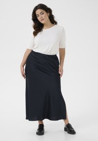 Top bianco a maniche corte abbinato a una lunga gonna blu navy fluente, con uno spacco laterale, indossato con scarpe nere testurizzate.