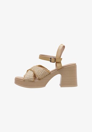Beige platform sandals with woven straw accents, wide cross straps, and an adjustable ankle strap. Features a chunky heel and textured sole.