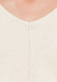 Hellbeige gestrickter Pullover mit V-Ausschnitt. Verfügt über eine subtile Textur und eine zentrale Naht, die vorne entlangläuft.