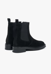 Czarne zamszowe botki Chelsea z elastycznymi panelami bocznymi i pętelką do podciągania. Płaska gumowa podeszwa i gładka faktura. Klasyczny krój do kostki.