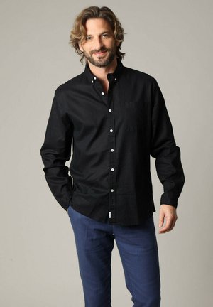 Chemise noire à boutons avec une poche, à manches longues et col. Fabriquée en tissu doux avec une texture lisse. Comprend des boutons blancs.