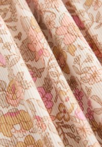 Blomstret stof med en cremefarvet baggrund og blomster i pink, brun og guld. Teksturen er ribbet, hvilket skaber et blødt, lagdelt udseende.