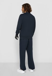 Marineblå genser og matchende joggebukser laget av myk tekstil. Komfortabel passform med ribbestrikkede mansjetter og ankelbeskjed. Hvite sneakers fullfører antrekket.