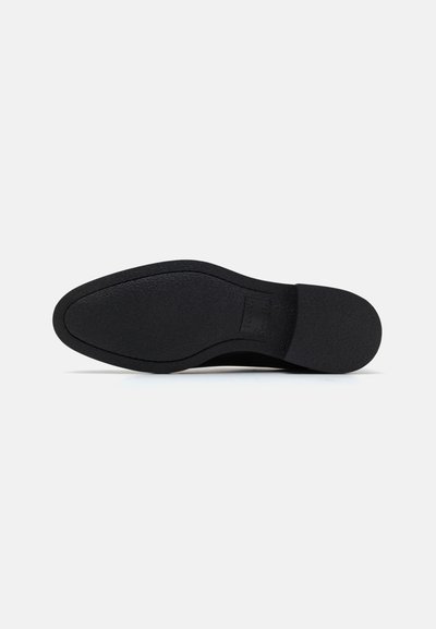 Semelle de chaussure noire avec une surface en caoutchouc texturé, légèrement courbée, talon renforcé et bord avant plat. Pas de marque visible.