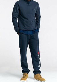 Tmavě modrá mikina s kulatým výstřihem, doplněná tmavě modrými tepláky s červeno-bílým logem "ELEMENT". Outfit doplňují béžové tenisky na šněrování.