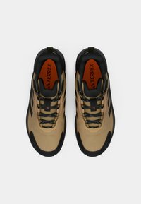 Beige turistické boty s černými akcenty, texturovaným svrškem a lace v modrém vzoru. Mají výrazný oranžový interiér a značkový logo.