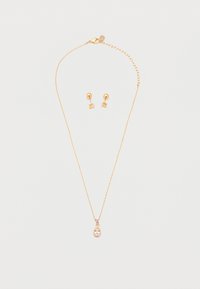 Χρυσό κολιέ με κρεμαστό μενταγιόν σε σχήμα δάκρυ με διαυγή πολύτιμη πέτρα και ταίριαστα χρυσά καρφωτά σκουλαρίκια με μικρές διαυγείς πέτρες σε λευκό φόντο.