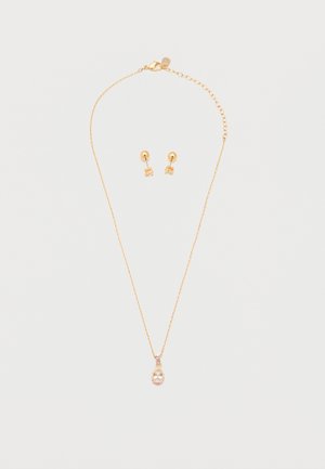 Zlatý náhrdelník s príveskom v tvare slzy z priehľadného drahokamu a zodpovedajúce zlaté náušnice s malými priehľadnými drahokamami na bielom pozadí.